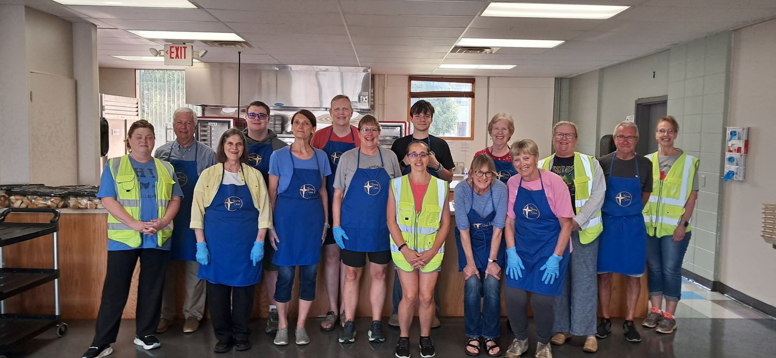 A group of smiling volunteers in blue aprons stand in the Sunshine Supper kitchen.